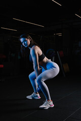 Fototapeta na wymiar Young woman with athletic body poses sexy with kettlebell. Young woman looks beautiful in the gym. Sporty woman looking at camera.