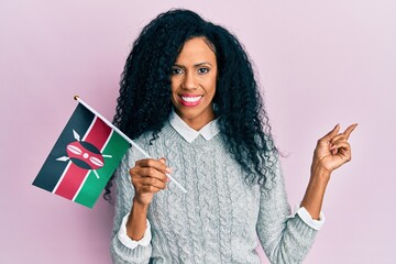 Middle age african american woman holding kenya flag smiling happy pointing with hand and finger to the side