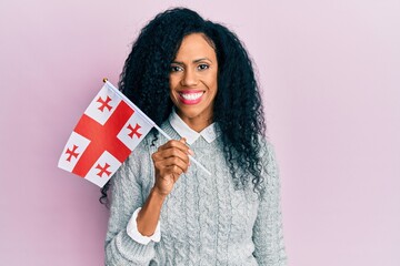Middle age african american woman holding georgia flag looking positive and happy standing and smiling with a confident smile showing teeth