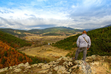 A man at the top of the mountain looks into the distance, against the background of mountains, sky and river. Clear sunny weather in the mountains