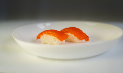 side view, on a gray and white background, a white plate with sushi, on rice-red fish