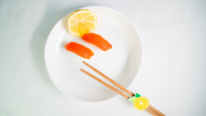 top view, white plate with sushi and lemon on a white background, red fish on rice, wooden chopsticks on a plate
