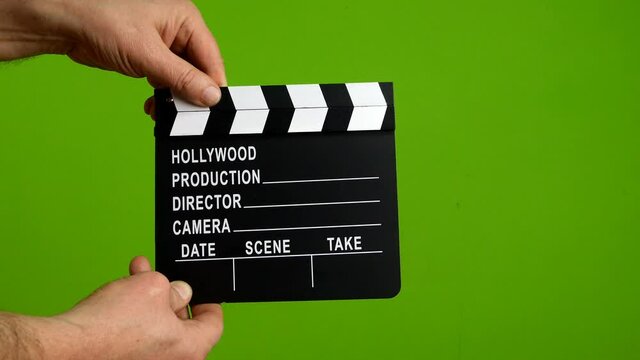 Human hands hold and clap with clapperboard. Beginning of scene in film or television production. Green screen. Chrome key. Close-up.