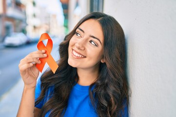 Young hispanic woman smiling happy holding orange ribbon at the city.