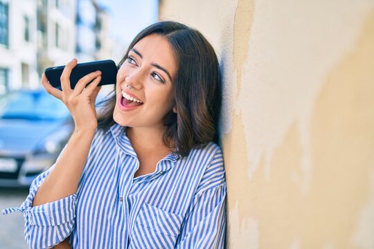 Young hispanic businesswoman smiling happy listening audio message using smartphone at the city.