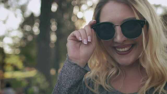 Plus size woman smiling in sunglasses. Closeup bokeh portrait. Nature landscape at summer sunny day. Surprising and flirt at park. Body positive girl. Blond model rest at green trees. Sun holiday walk