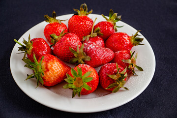 Appetizing juicy bright strawberries on a white plate on a black background - vitamin composition, taste of summer