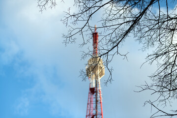 Blurred background. Telecommunication tower in blurry focus against a blue sky, in focus of a tree branch, cell antenna, transmitter. TV tower