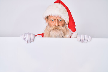 Naklejka premium Old senior man with grey hair and long beard wearing santa claus costume holding banner skeptic and nervous, frowning upset because of problem. negative person.