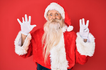 Old senior man with grey hair and long beard wearing traditional santa claus costume showing and pointing up with fingers number eight while smiling confident and happy.