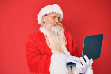 Old senior man with grey hair and long beard wearing santa claus costume using laptop depressed and worry for distress, crying angry and afraid. sad expression.