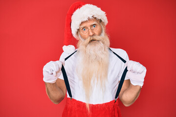 Fototapeta na wymiar Old senior man wearing santa claus costume with suspenders in shock face, looking skeptical and sarcastic, surprised with open mouth