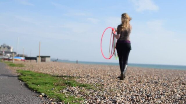 Una mujer rubia recogiendo unos aros de hula hoop del suelo de una playa en un d&iacute;a soleado