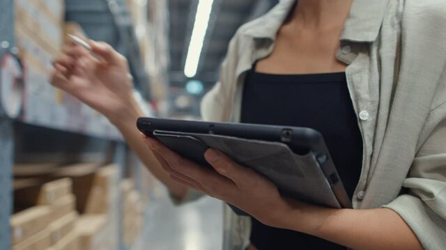 Attractive young Asia businesswoman manager looking for goods using digital tablet checking inventory levels standing in retail shopping center. Distribution, Logistics, Packages ready for shipment.