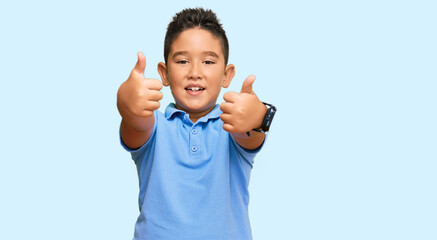Little boy hispanic kid wearing casual clothes success sign doing positive gesture with hand, thumbs up smiling and happy. cheerful expression and winner gesture.
