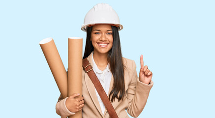 Beautiful hispanic woman holding paper blueprints surprised with an idea or question pointing finger with happy face, number one