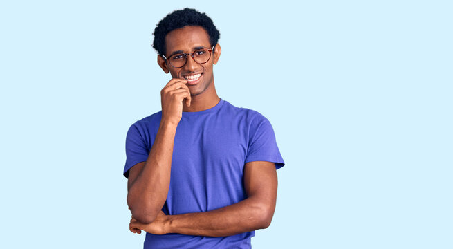 African handsome man wearing casual clothes and glasses looking confident at the camera with smile with crossed arms and hand raised on chin. thinking positive.