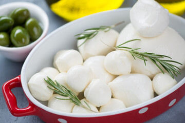 Close-up of mozzarella balls of different sizes with fresh rosemary and green olives, selective focus