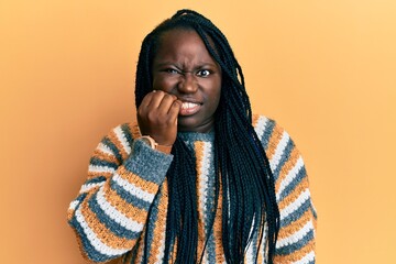 Young black woman with braids wearing casual winter sweater looking stressed and nervous with hands on mouth biting nails. anxiety problem.