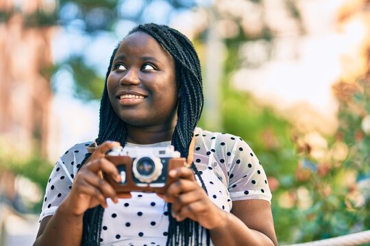 Young african american tourist woman smiling happy using vintage camera at the city.