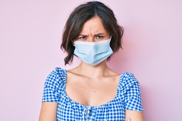 Young beautiful woman wearing medical mask skeptic and nervous, disapproving expression on face with crossed arms. negative person.