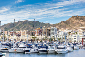 Fototapeta na wymiar Beautiful Benalmadena touristic Harbour. Boats and yachts docked in the port. in background luxury urbanisations and hotels. Sunny summer day, blue sky with some clouds. 