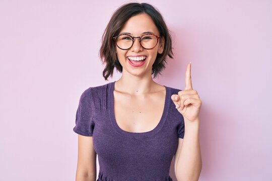 Young beautiful woman wearing casual clothes and glasses pointing finger up with successful idea. exited and happy. number one.