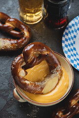 Pretzels with cheese dipping sauce and beer, vertical shot on a brown stone background
