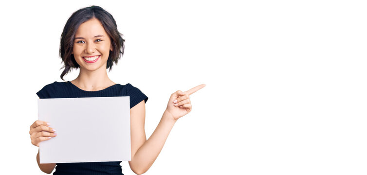 Young beautiful girl holding blank empty banner smiling happy pointing with hand and finger to the side