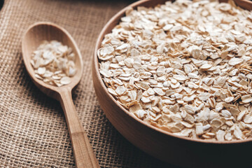 Dry oatmeal in a wooden bowl and spoon on a linen fabric background. Copy, empty space for text