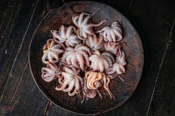 Raw baby octopus in a wooden plate. Organic seafood. Top view.  © Adsloboda
