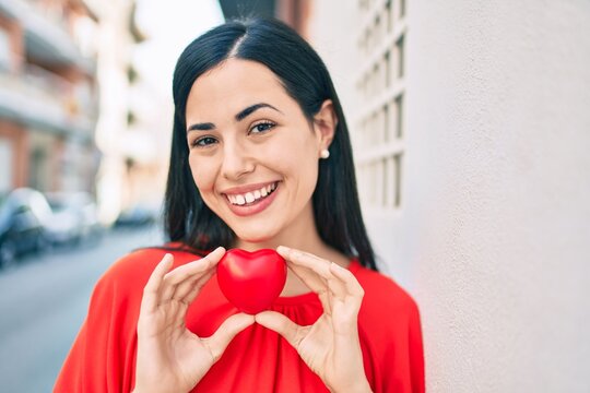 Young latin girl smiling happy holding heart at the city.