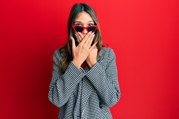 Young brunette woman wearing fashion and modern look shocked covering mouth with hands for mistake....