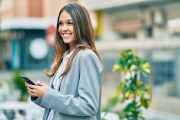 Young latin businesswoman smiling happy using smartphone at the city.
