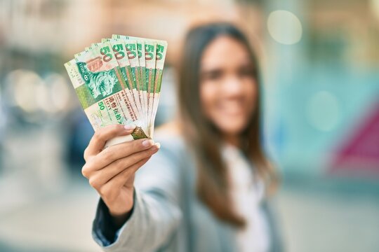 Young latin businesswoman smiling happy holding hong kong dollars at the city.