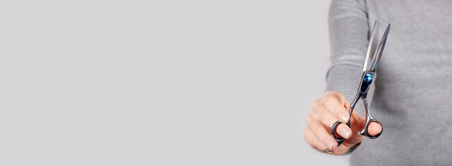Hand with thinning scissors on grey background.