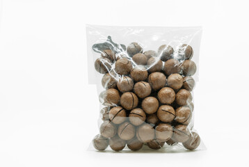 Macadamia nuts in shell and cracker tool in cleared plastic packaging on white background. Isolated...