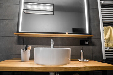 Bathroom interior with grey tile on a wall, stylish round sink and tap on a oak wood worktop. Minimalism in interior of bathroom.