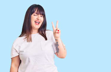 Young plus size woman wearing casual clothes smiling with happy face winking at the camera doing victory sign with fingers. number two.