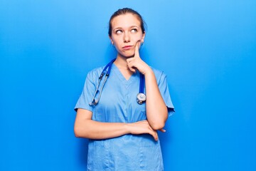 Young blonde woman wearing doctor uniform and stethoscope serious face thinking about question with...