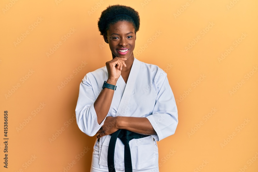 Poster Young african american girl wearing karate kimono and black belt looking confident at the camera with smile with crossed arms and hand raised on chin. thinking positive.