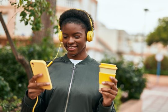 Young african american girl drinking coffee using smartphone and headphones at the city