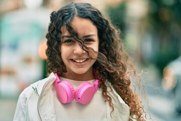 Fototapeta premium Hispanic child girl smiling happy using headphones at the city.