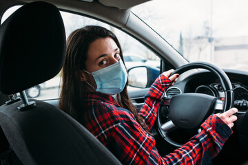 Young woman with disposable face mask sitting in a car