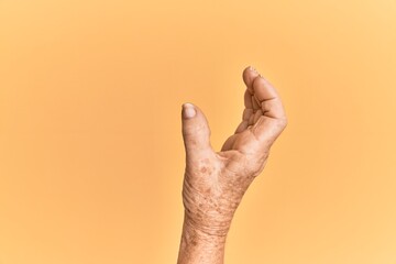 Senior caucasian hand over yellow isolated background picking and taking invisible thing, holding object with fingers showing space
