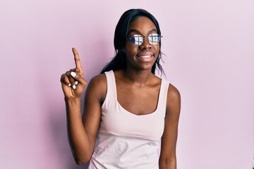 Young african american woman wearing casual clothes and glasses smiling with an idea or question pointing finger up with happy face, number one