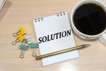 The word solution is written on a notepad that lies next to a white coffee cup and colored stationery clips