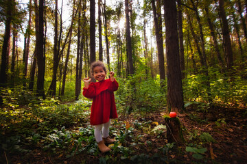 A little African-American girl in a red dress in the woods with a red apple.