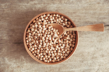 Raw chickpeas in a wooden plate and spoon on an rustic wooden background. Top view. Copy, empty space for text