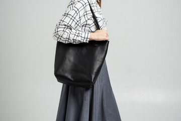 Small black leather bag in a woman's hand on a white background. Shoulder handbag. Woman in a white...